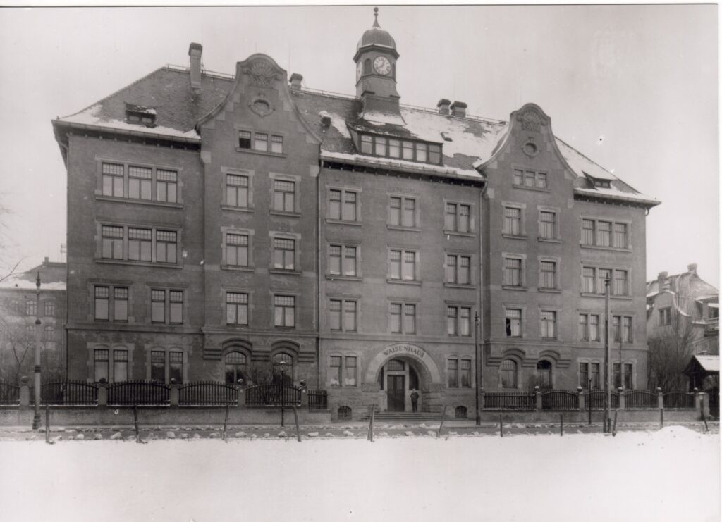 Das Waisenhaus kurz nach der Eröffnung 1903. Ein Zaun umgibt das Haus, der alte Uhrenturm steht noch. Rund um den Eingang steht das Wort "Waisenhaus".